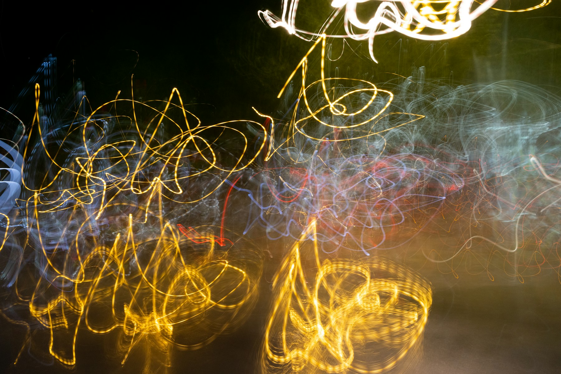 Gold, blue, and white light trails moving across darkness